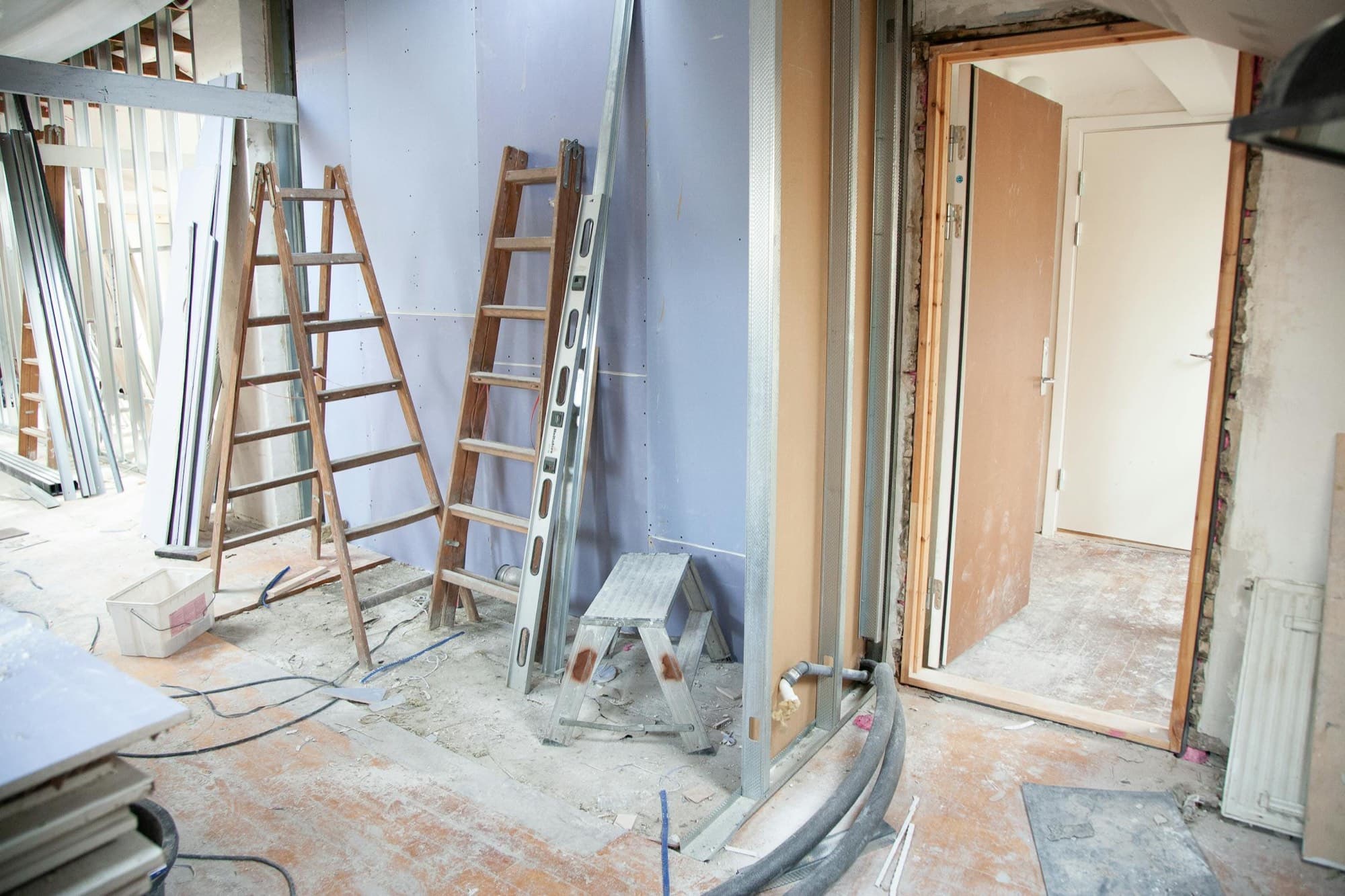 Interior remodel in progress: metal stud framing, drywall, and ladders